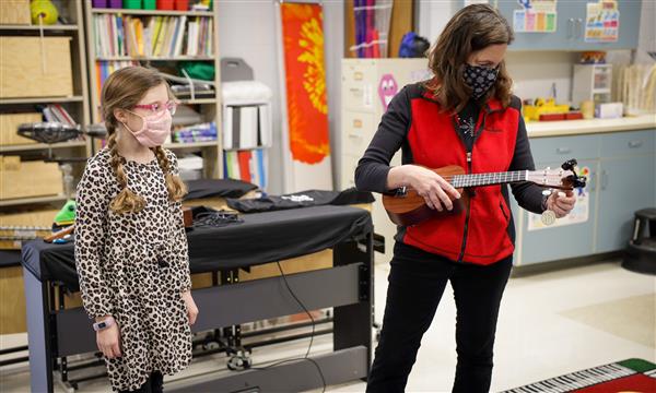 teacher tunes ukulele as student watches